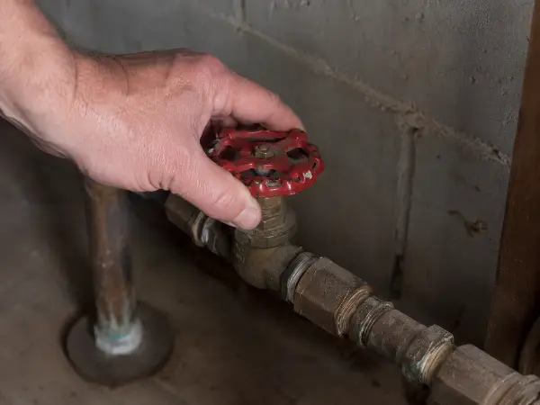 Mano cerrando la válvula principal de agua tras una tubería rota